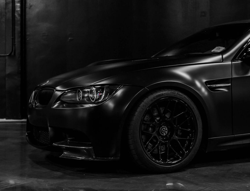 Black sports car parked in a dark garage, front-left view with glossy finish and custom rims