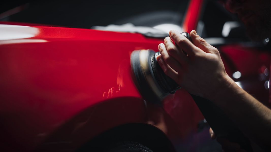 Hands polishing a red car with a cloth or buffer in a dark garage