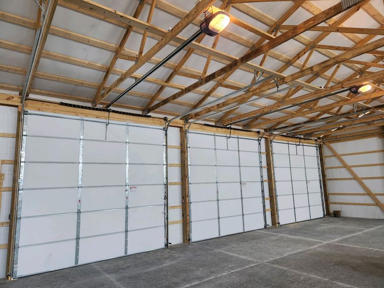 Empty warehouse interior with white roll-up doors, wood truss ceiling, and concrete floor