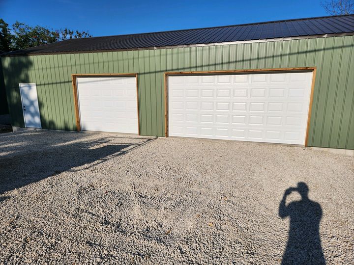 Green garage building with two white doors and gravel driveway in bright sunlight