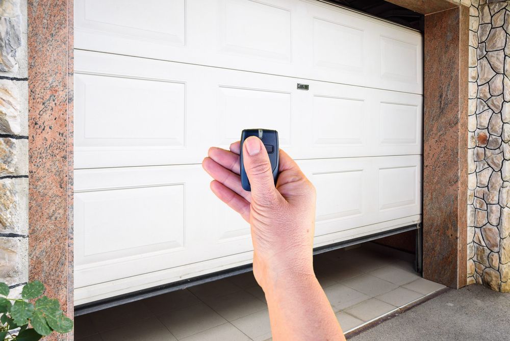 Hand holding a garage door opener toward a white garage door opening slightly