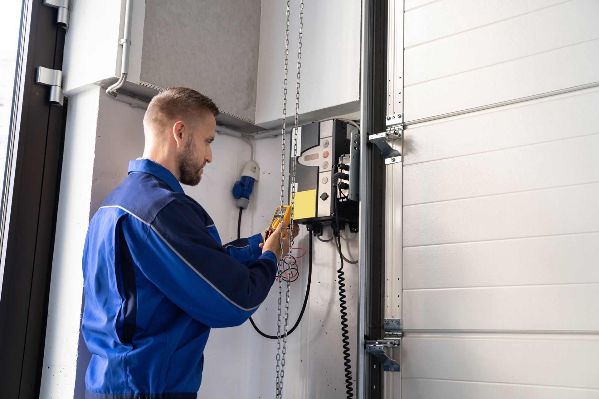 Worker in blue uniform operating a control panel beside an industrial garage door