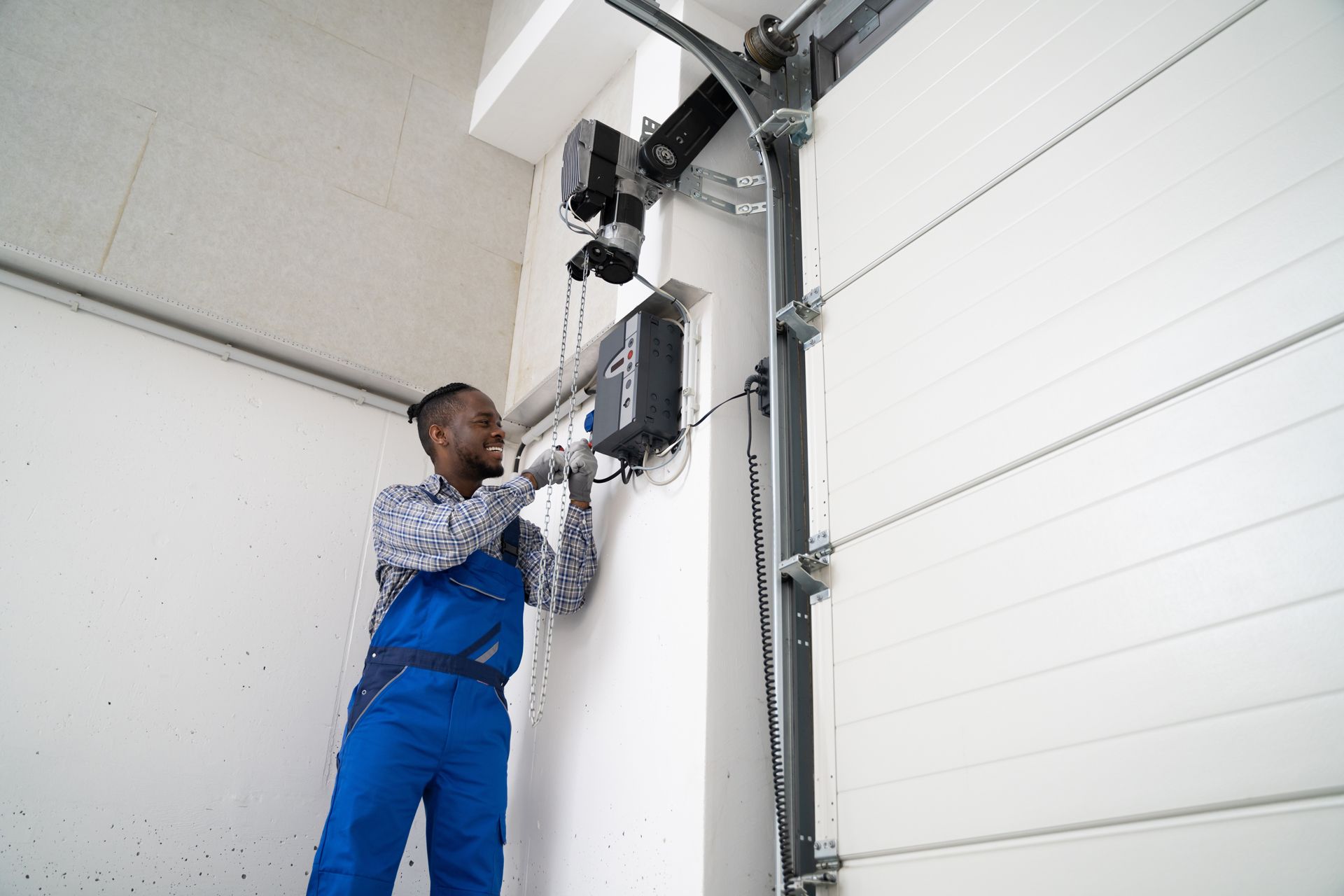 Technician in blue overalls repairing a garage door opener on a white sectional door