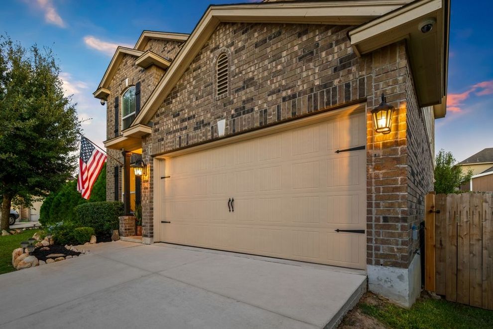 Suburban brick house with two-car garage, concrete driveway, and American flag by the front porch