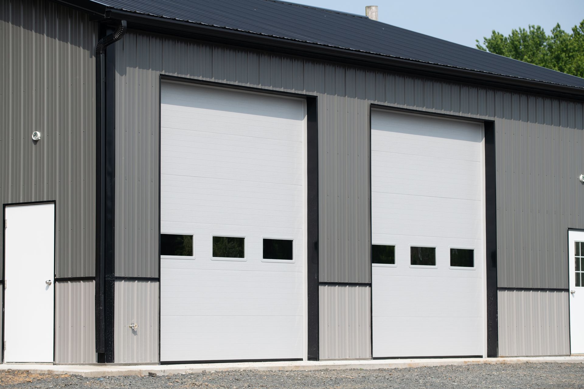 Gray industrial building with two white roll-up garage doors and a side entry door