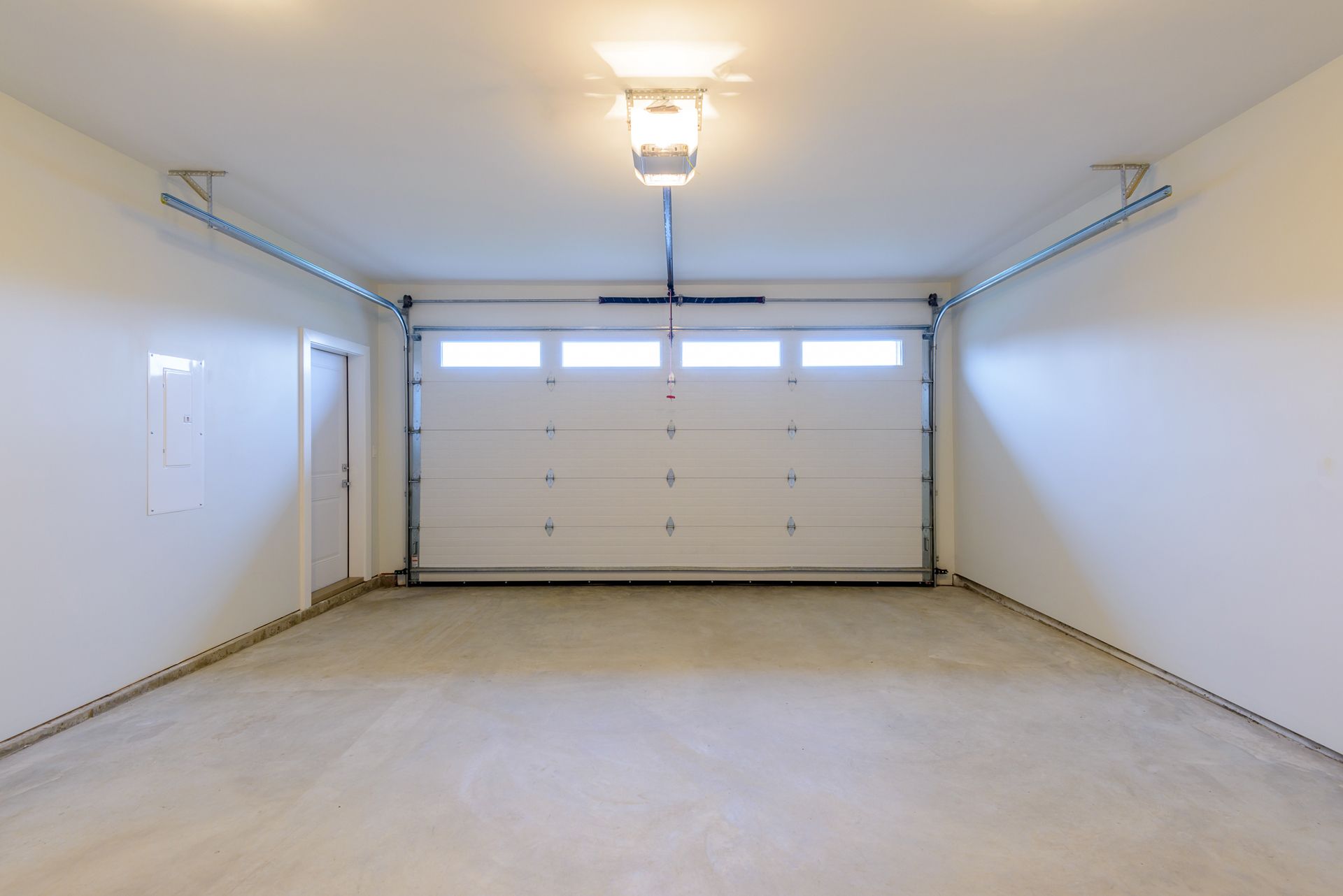 Empty white garage with closed door, concrete floor, and overhead light