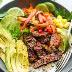 A close up of a bowl of food with meat , rice , avocado and vegetables.