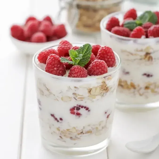 Two glasses of yogurt with raspberries and mint on top