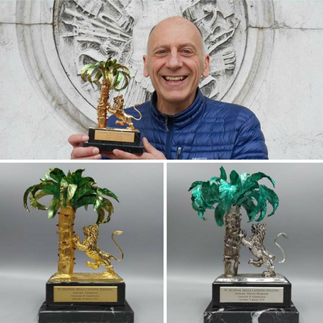 Vari trofei d'argento e d'oro esposti all'aperto su un tavolo con uno sfondo verde sfocato.