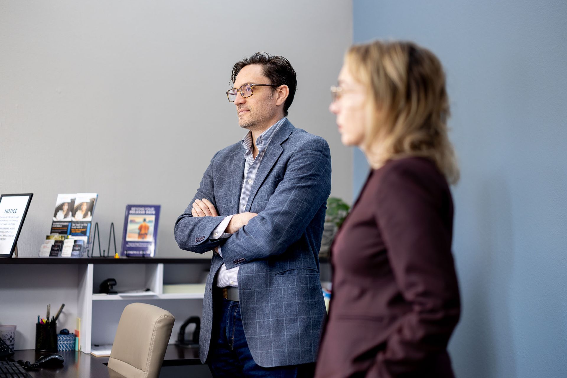Shellie and Ken standing in an office, one with arms crossed, shelves and framed items in the background