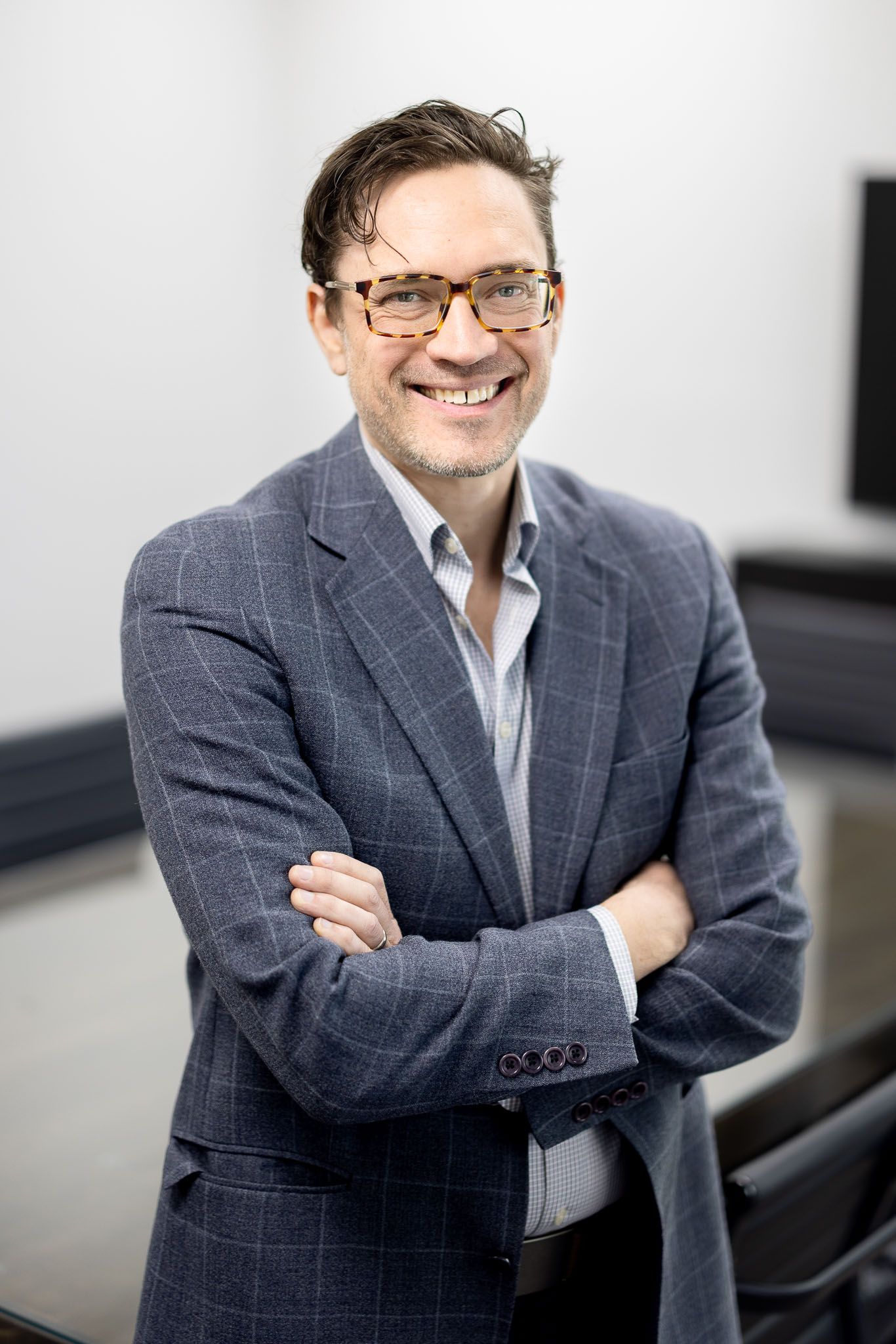 Kenin a blue blazer and glasses standing with arms crossed, smiling in an office setting