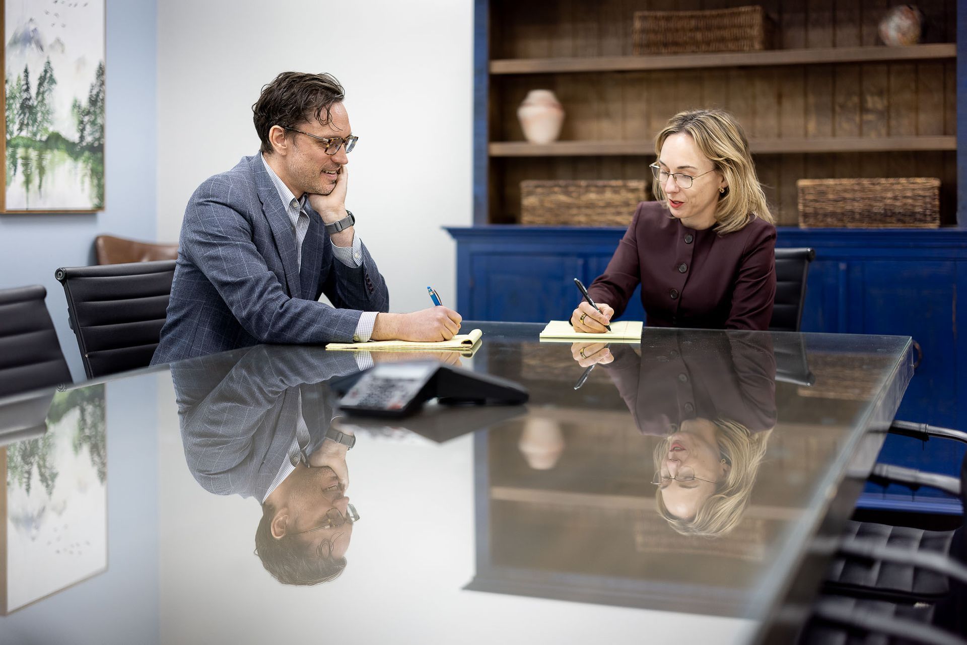 Ken and Shellie writing notes across a conference table in a modern office meeting room