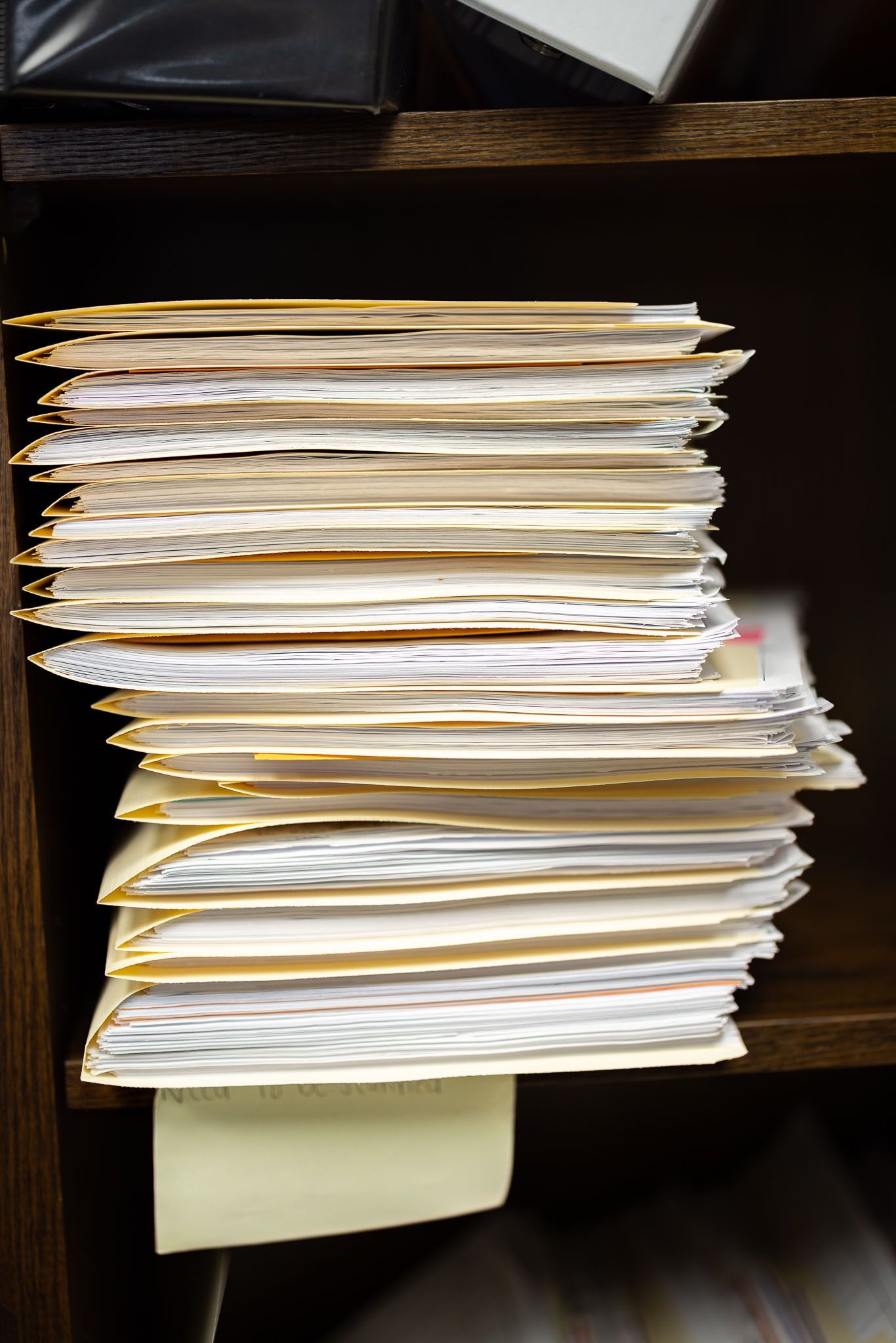 Stack of papers on a shelf, with loose sheets protruding in a cluttered file organizer.