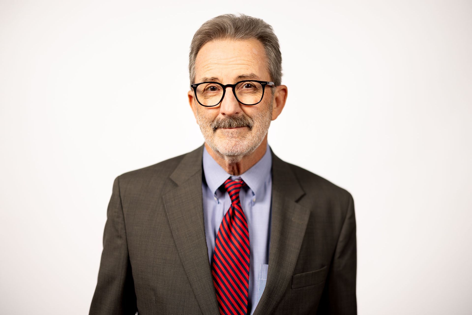 Portrait R. Brent Capshaw in a brown suit, red tie, and glasses against a plain white background