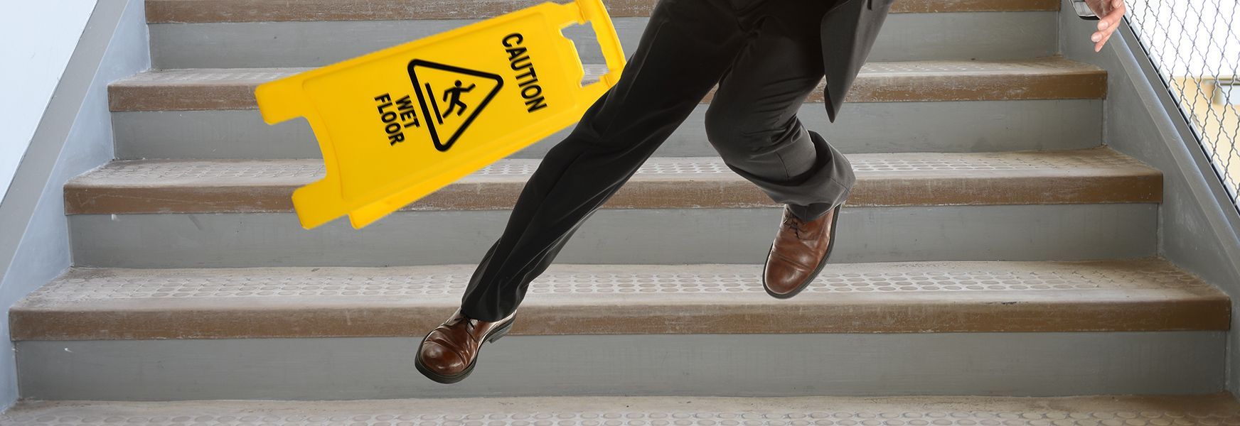 Person slipping on stairs near yellow caution sign.