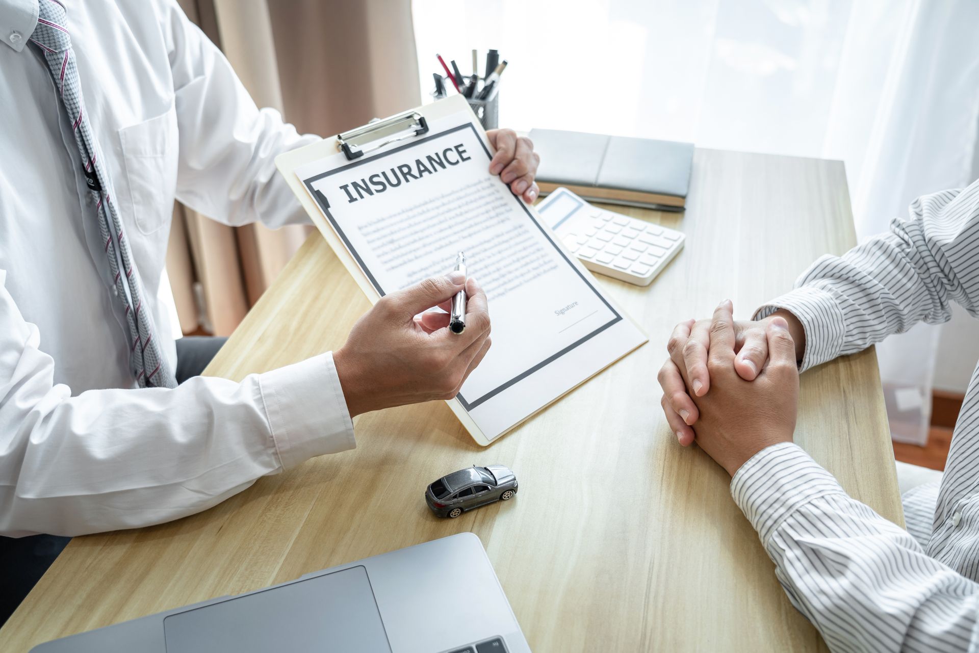 Insurance agent reviewing documents with a client at a desk, hands clasped during consultation