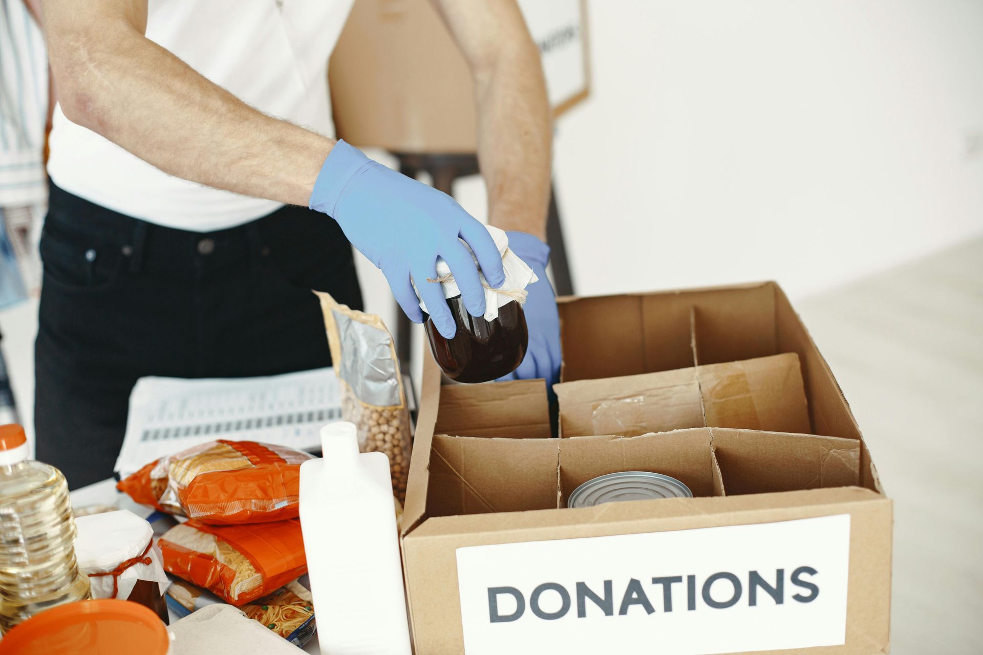Gloved hands sorting items into donation boxes on a table with food and supplies
