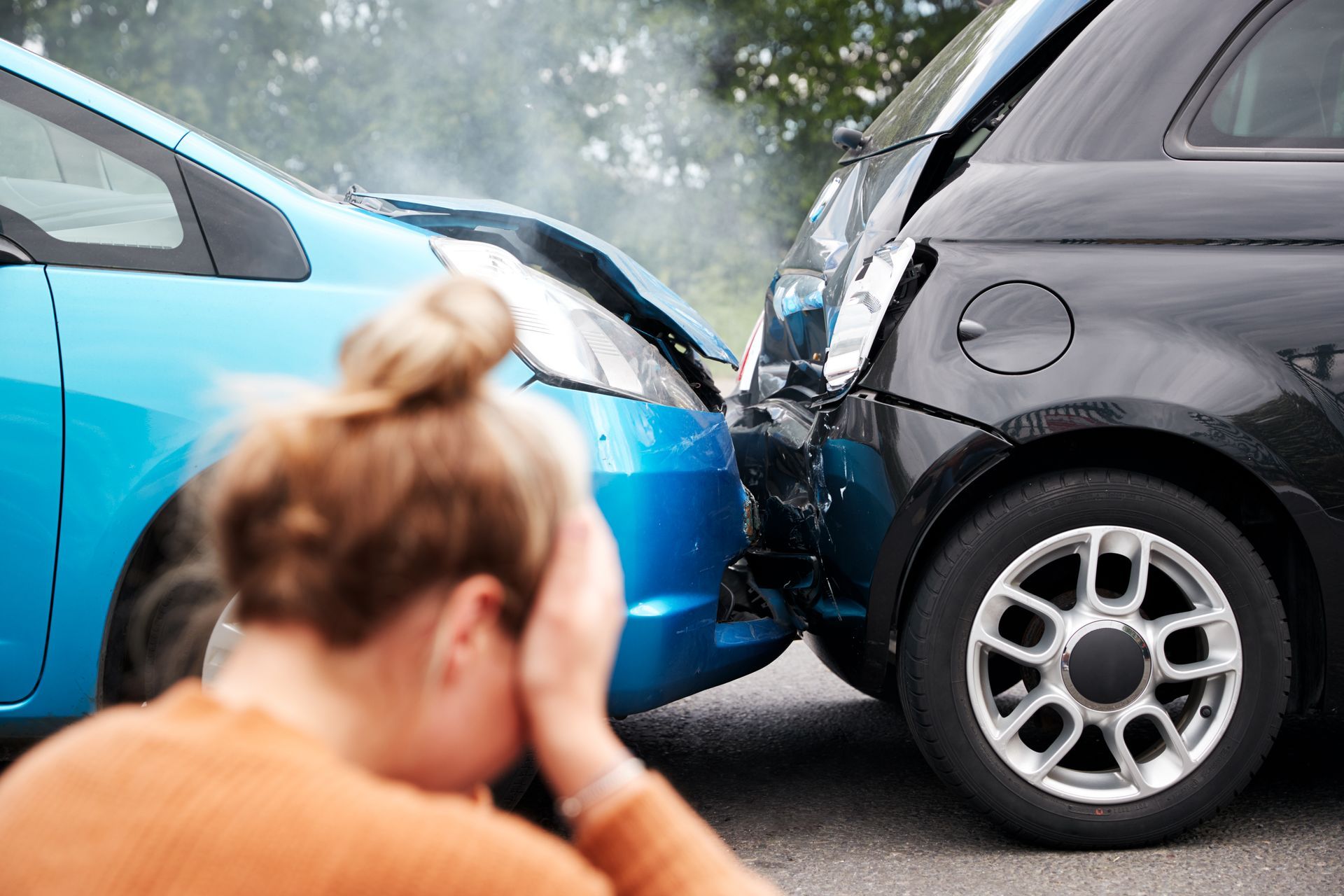 Two cars collide head-on on a road, with a person in the foreground holding their head.