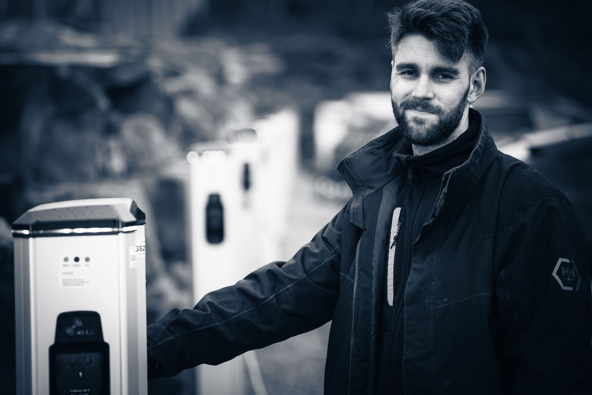 A person stands next to a row of modern electric vehicle charging stations, smiling toward the camera.