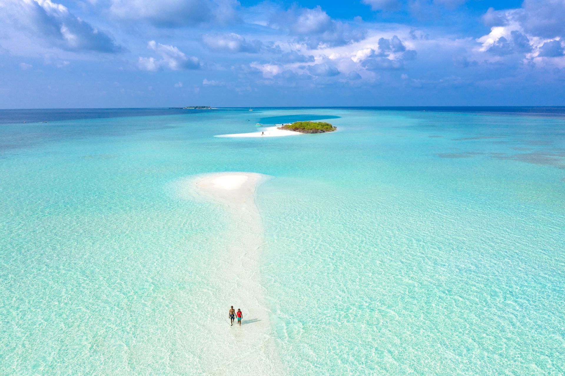 An aerial view of a couple walking on a sandy beach in the ocean.