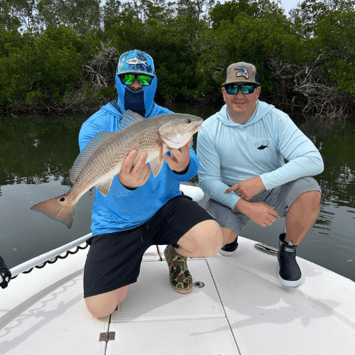 Two men are kneeling on a boat holding a large fish.