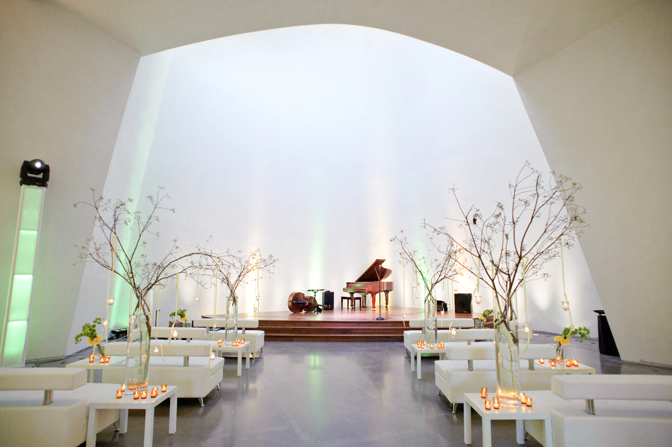 Weding reception setup with white tables and a piano on the stage.