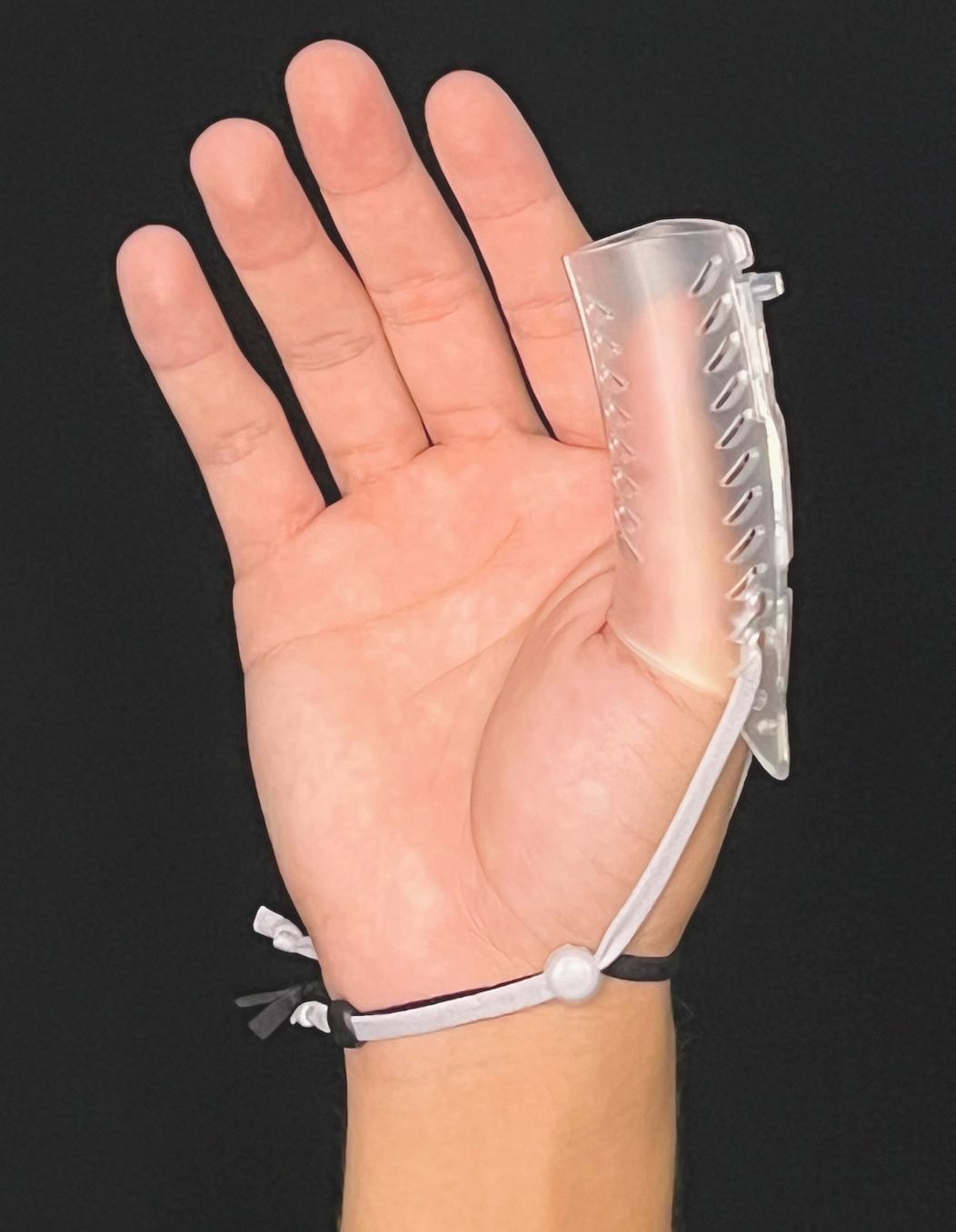 Hand with a DigiTube clear plastic finger splint and wrist strap on a dark background