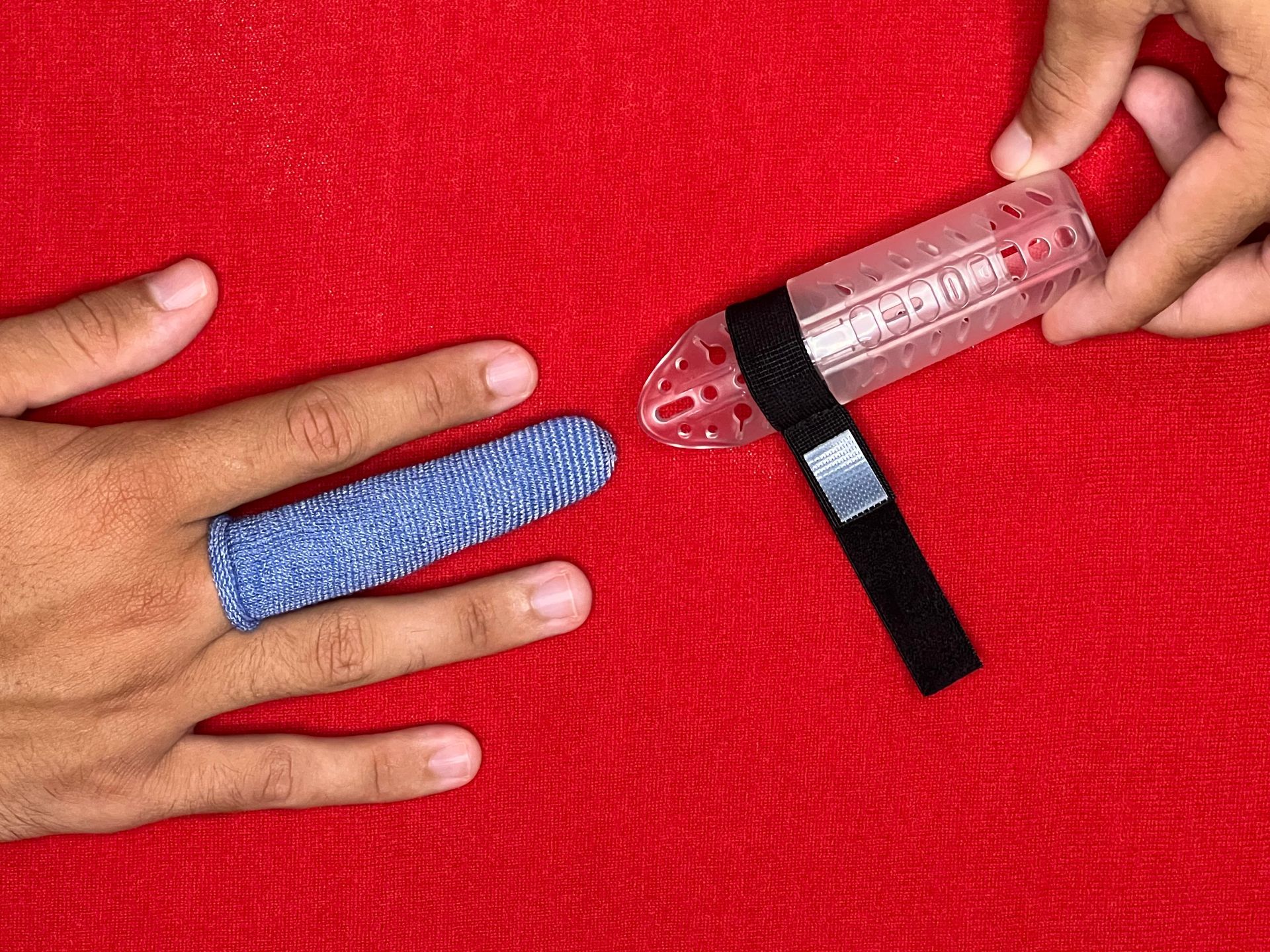 Hands with a blue finger wrap and a DigiTube clear plastic finger splint on a red background