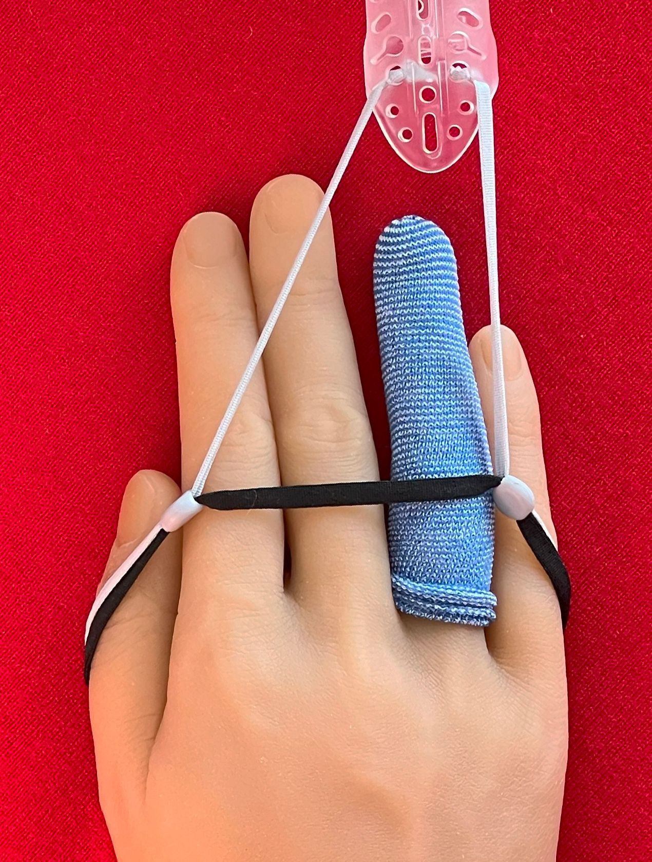 Hand with DigiTube blue finger splint and black strap secured by a white cord on a red background