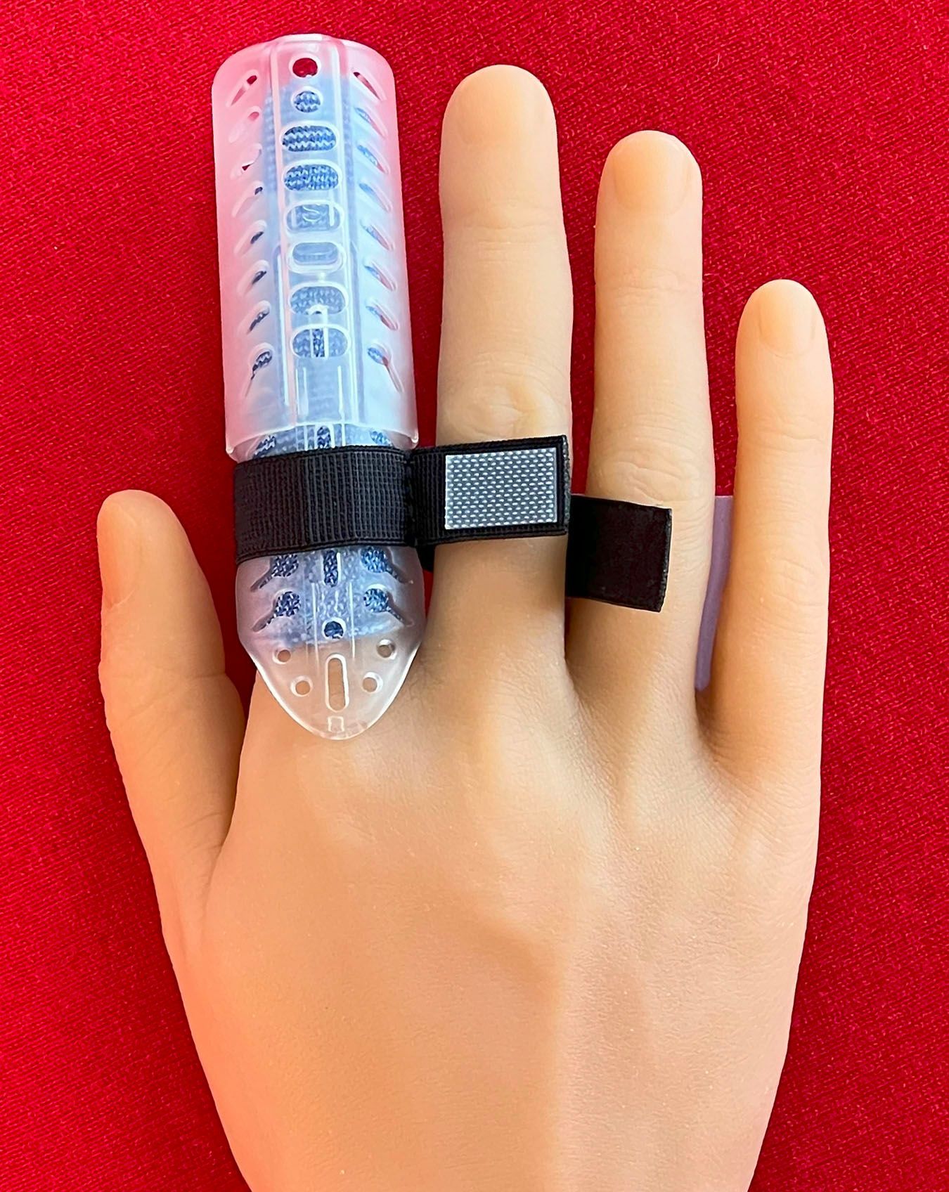 Hand with a DigiTube clear plastic finger splint strapped on, against a bright red background.