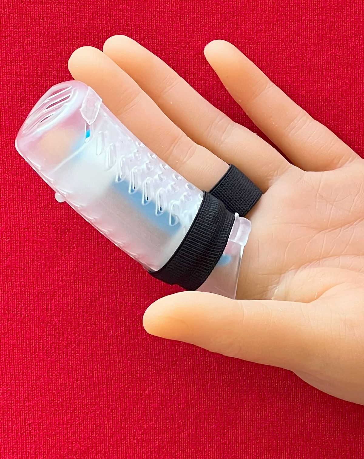 Hand wearing a DigiTube transparent finger splint with black straps on a red background