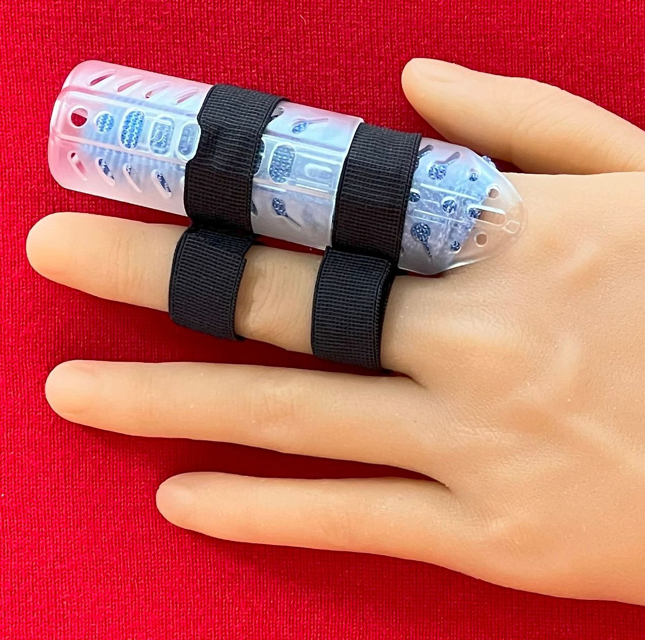 Hand with DigiTube black finger splint and clear-blue protective finger cap against a red background