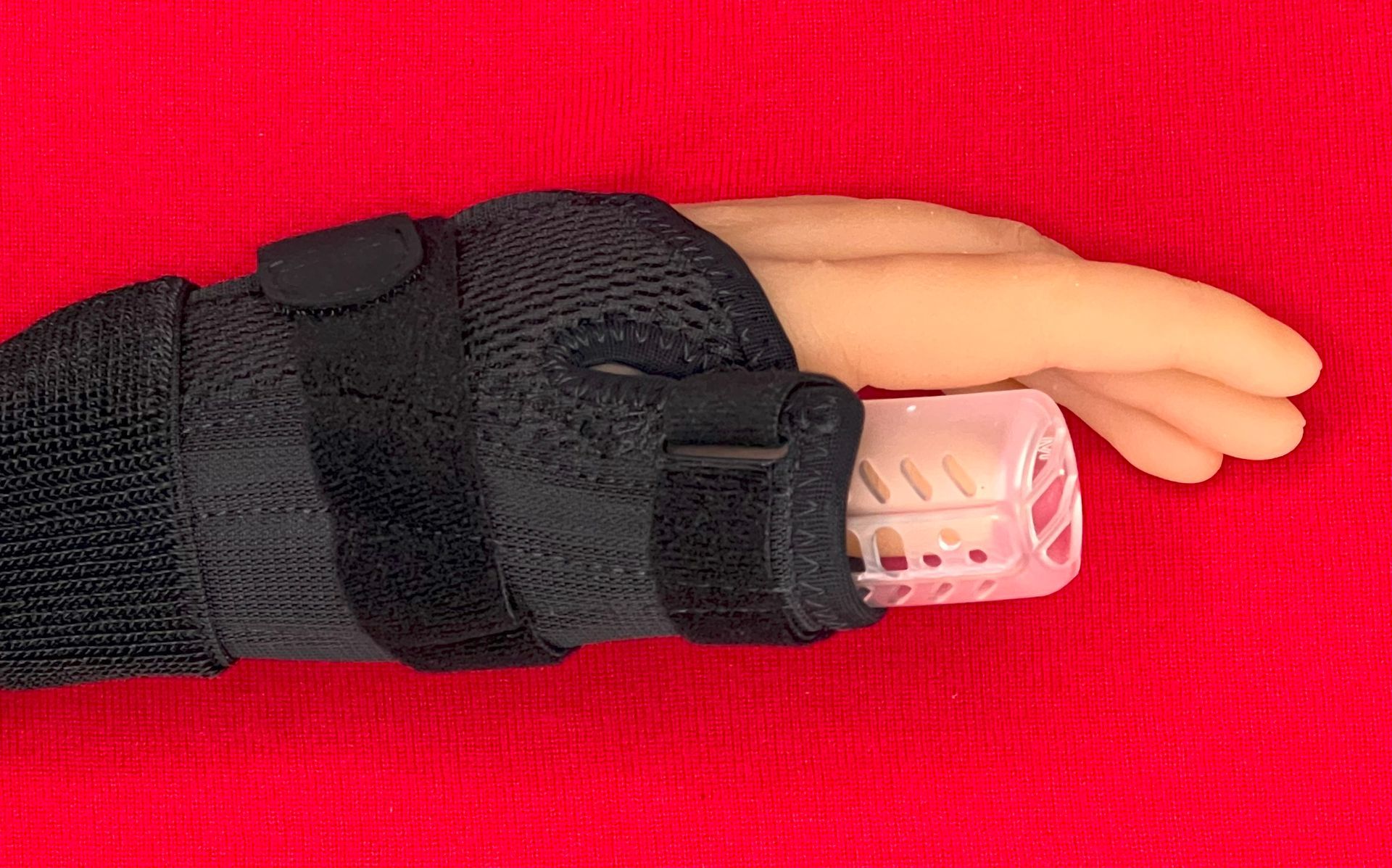 Close-up of a hand in a black glove holding a DigiTube thumb guard against a red background