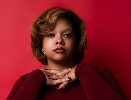 Portrait of a person in a burgundy top against a bright red background, resting hands under chin