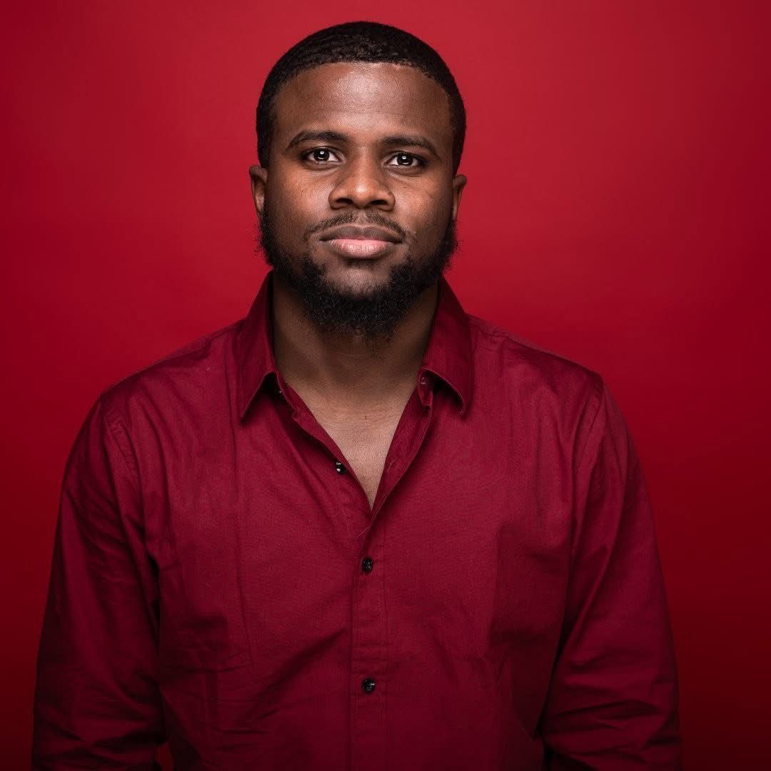 Man in a red button-up shirt against a plain red background, facing forward with a neutral expression