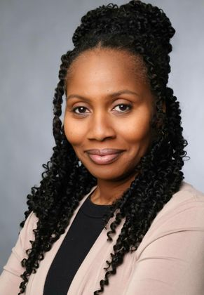 Portrait of a smiling woman with long curly hair wearing a beige blazer against a gray background