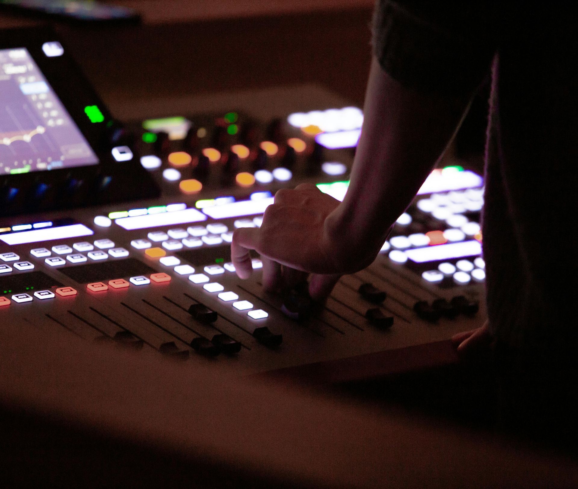 Hand adjusting controls on a lit audio mixing console in a dark studio