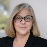 Woman with blonde bob and glasses wearing a black blazer, looking at the camera.