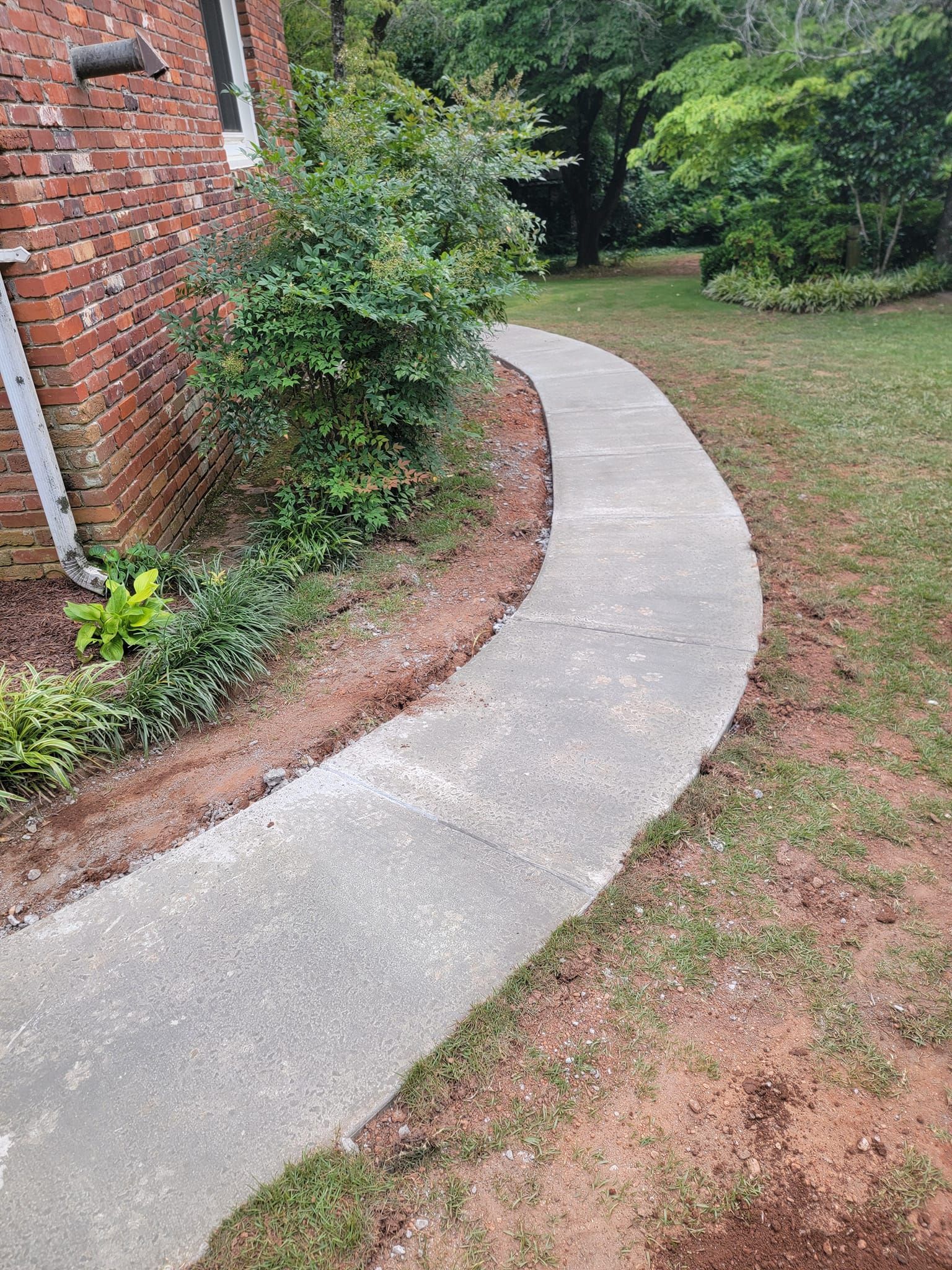 Curving concrete sidewalk beside a brick building and grassy yard.
