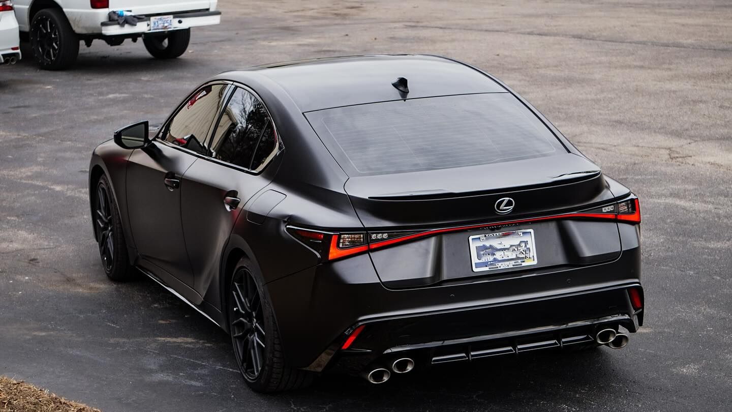 Black Lexus coupe from rear. Tail lights are lit. Parked outside.