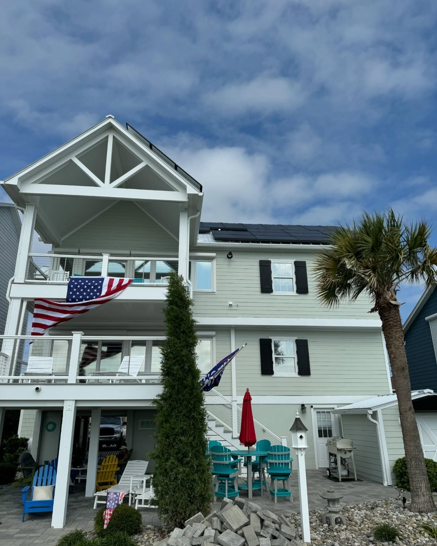 Beach house with solar panels, American flag, palm tree, blue sky.