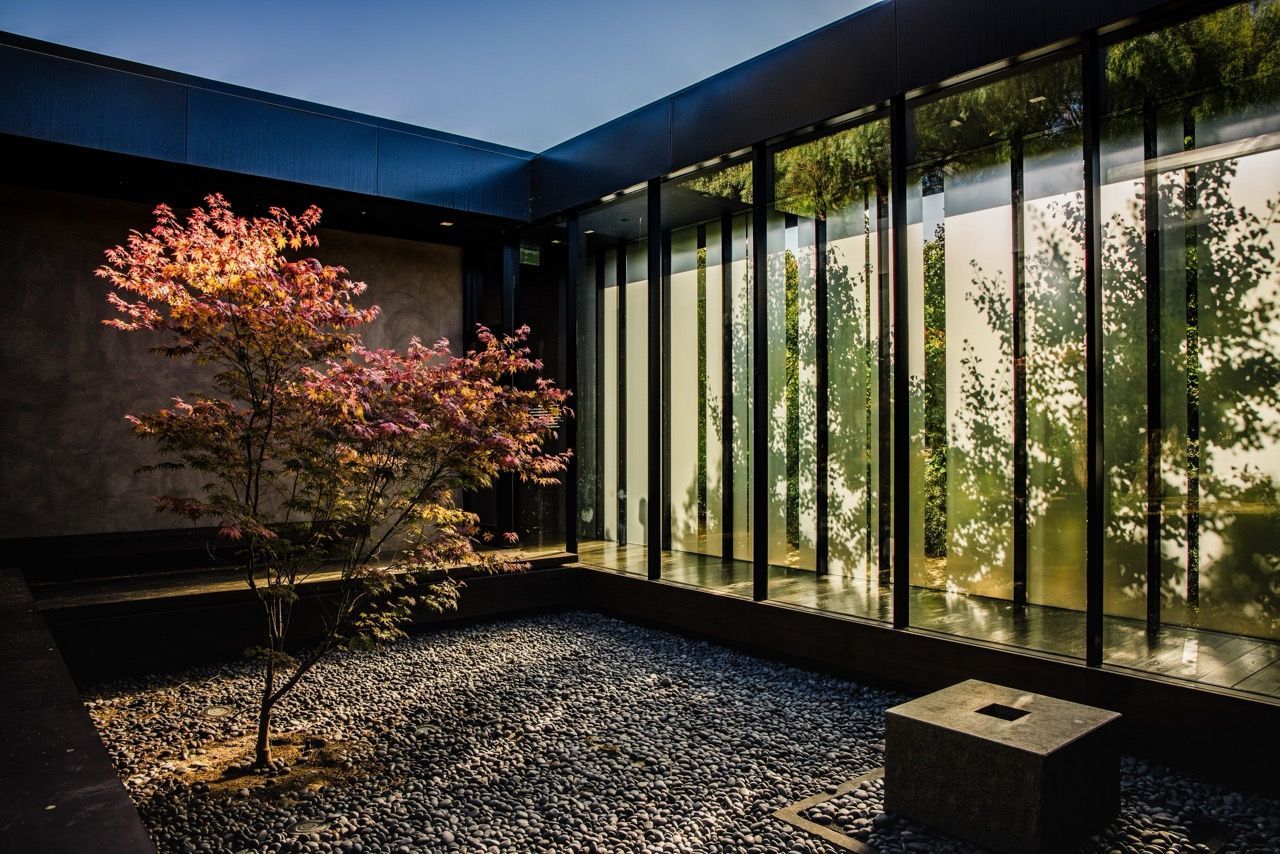 A small courtyard with a pink tree, gravel floor, and glass wall showing trees.