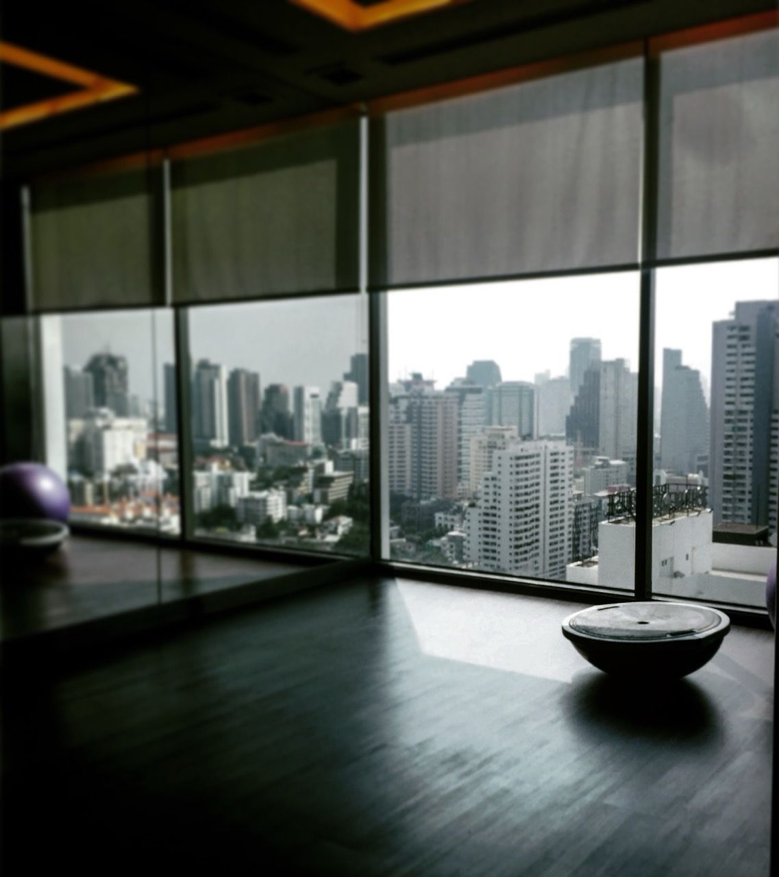 Room with a city view through large windows; a dark floor and exercise ball are visible.
