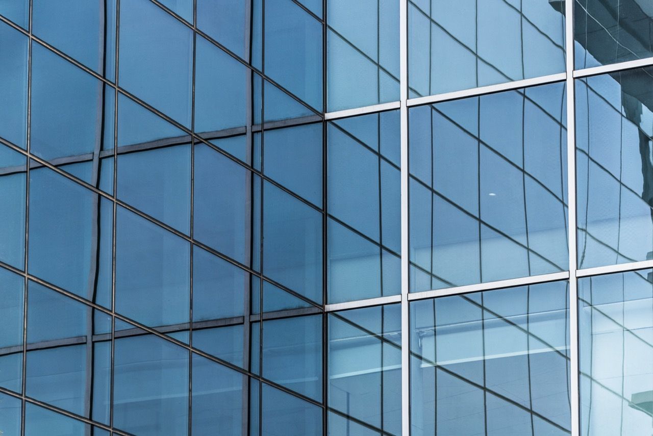 Glass facade of a modern building reflecting blue sky. White grid pattern frames the windows.