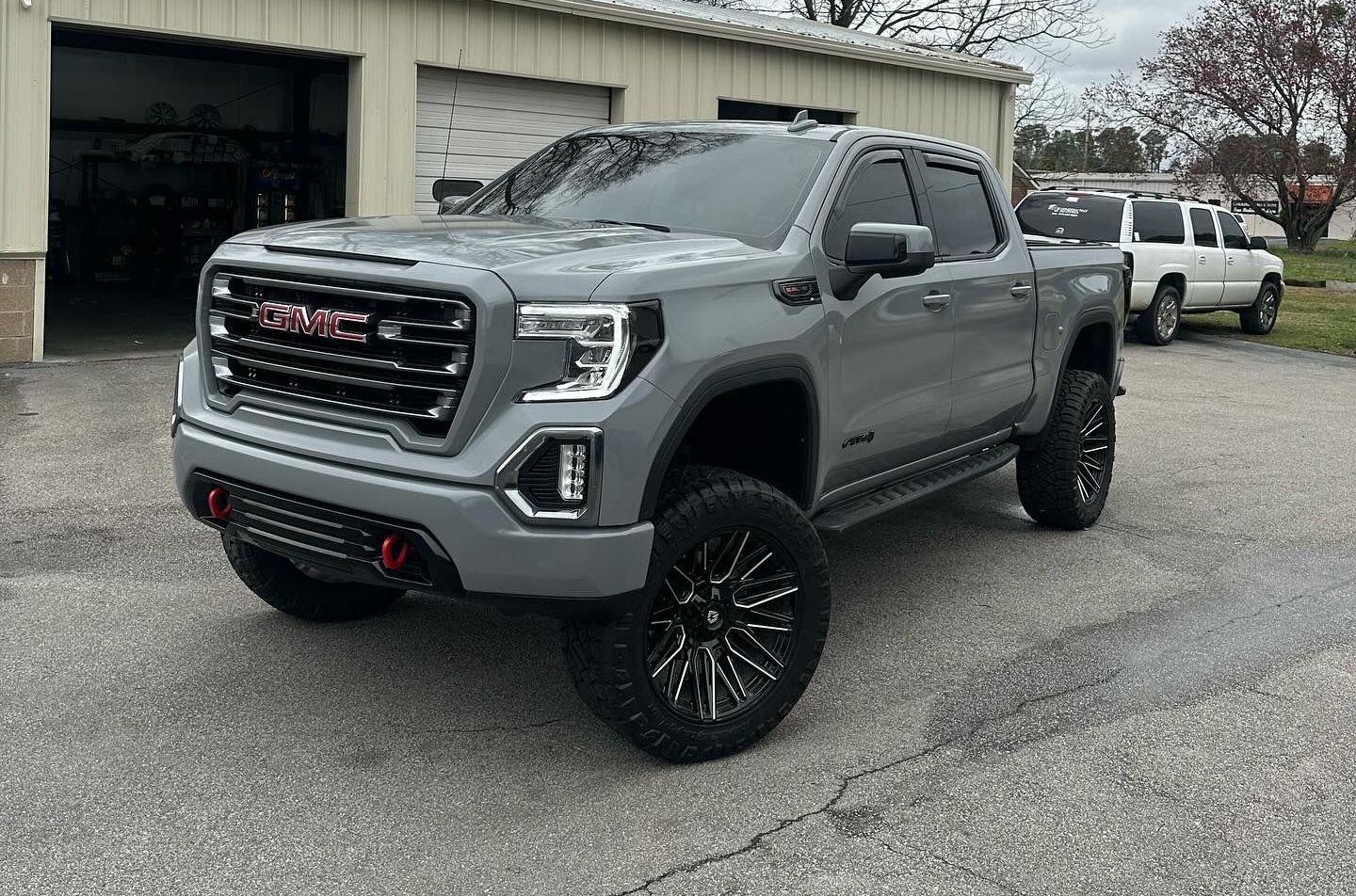 Gray GMC truck, black wheels, parked in front of a garage.