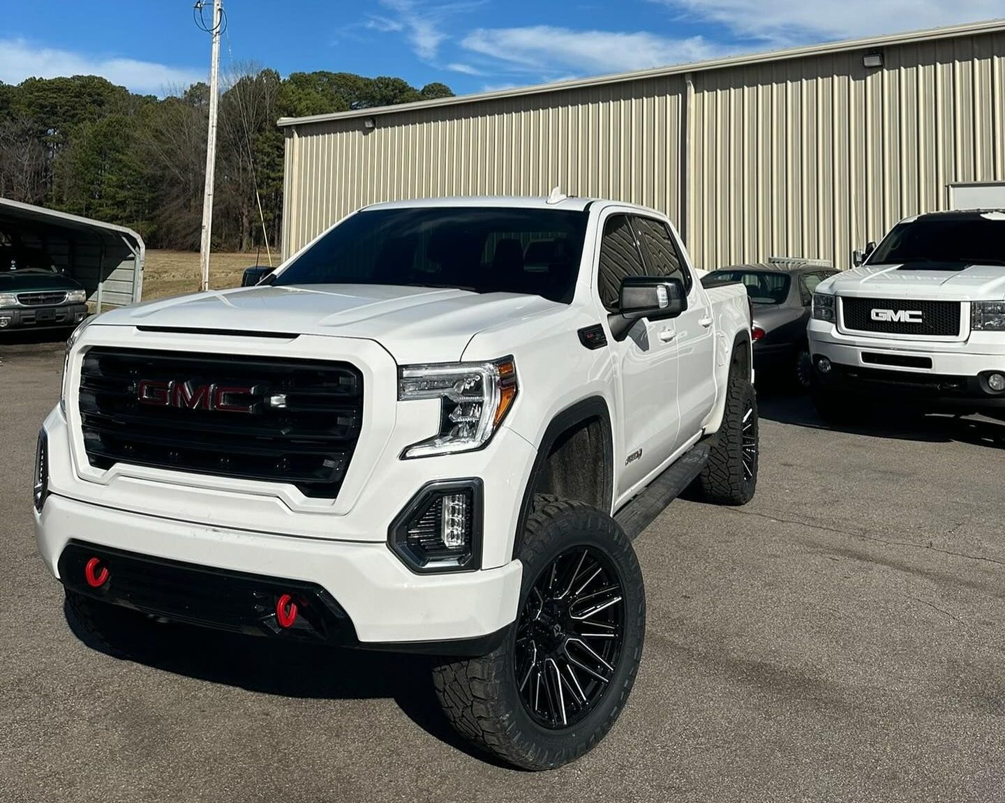 White GMC truck with black rims and tinted windows parked outside a building.