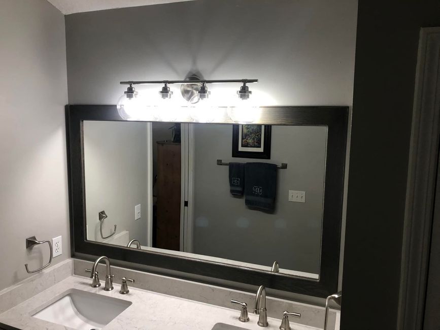 Bathroom vanity with large mirror, wall lights, and gray walls over a white countertop sink.