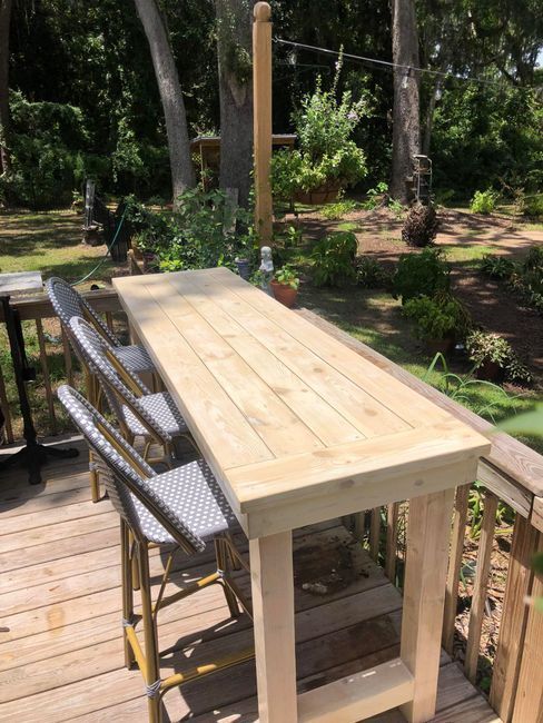 Wooden outdoor table and chairs on a deck overlooking a leafy garden
