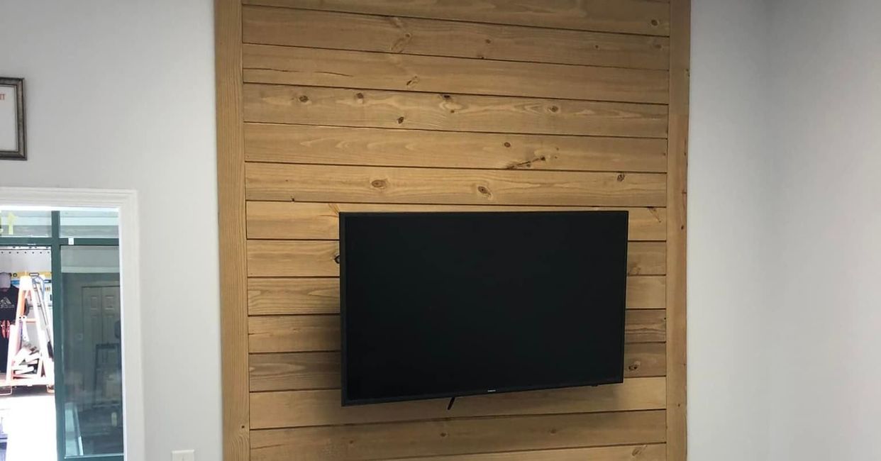 Wall-mounted black TV on a light wood slat accent wall in a bright room.