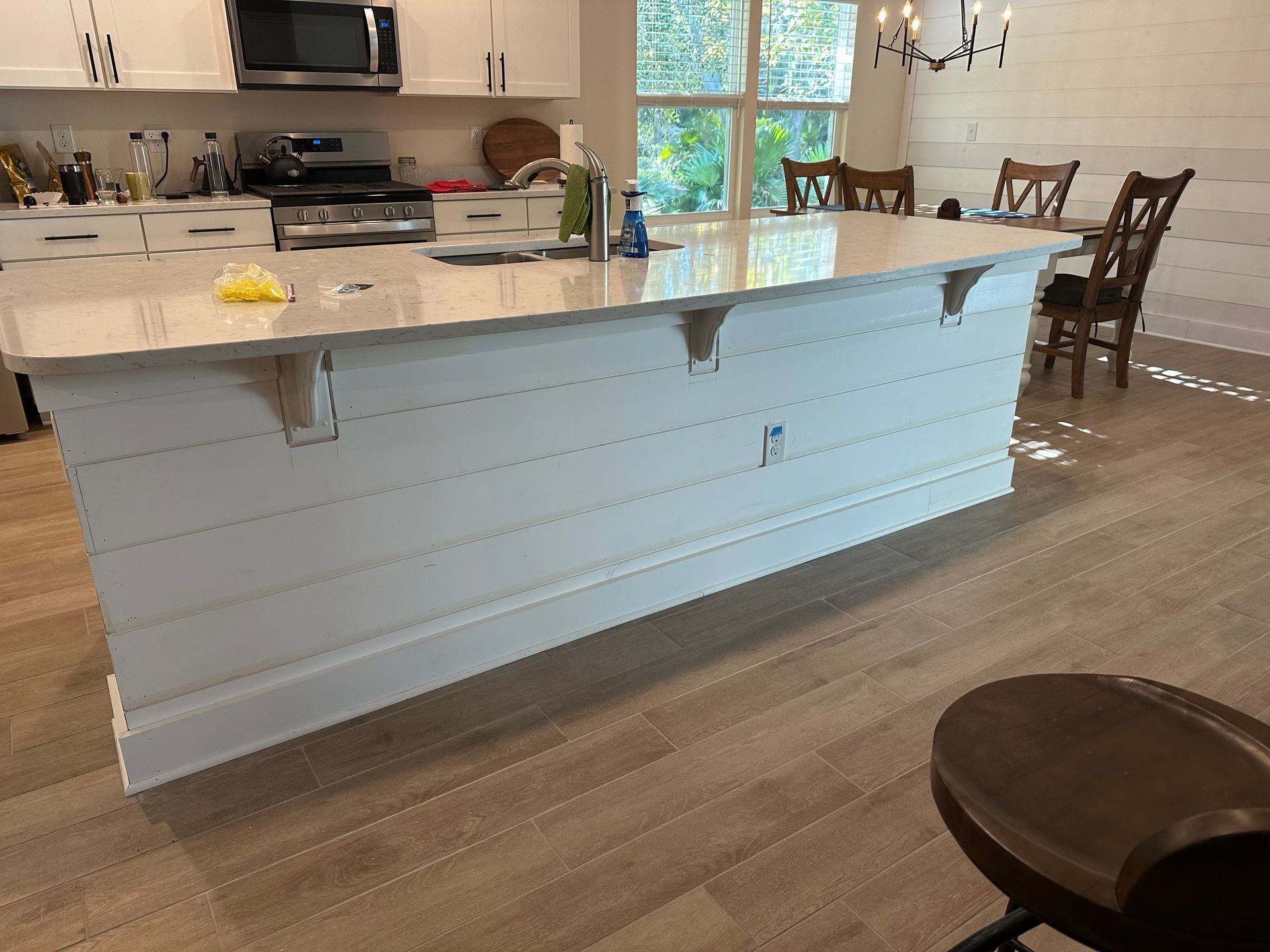 Bright kitchen with white island, marble countertop, wooden floor, and dining table by a sunlit window
